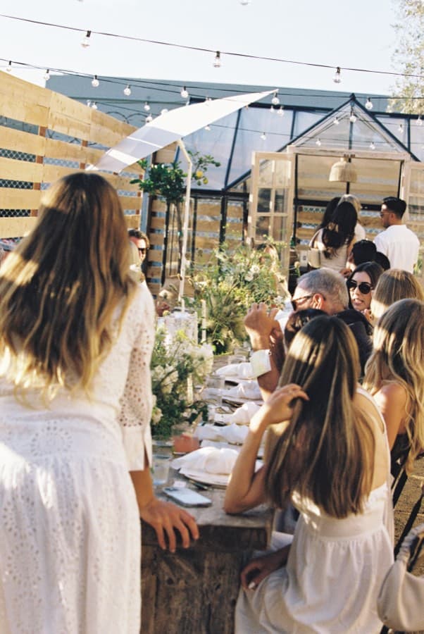 Guests in white gathered at a long outdoor table under string lights