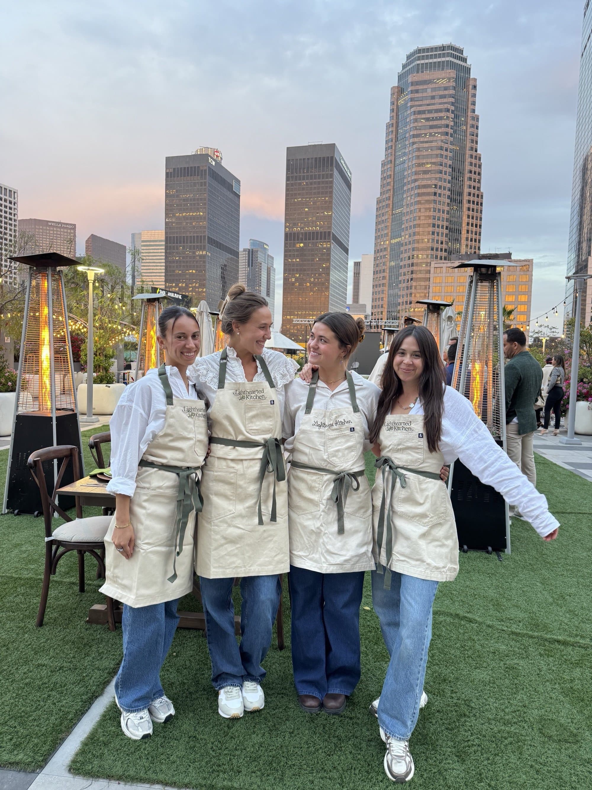 Four Lighthearted Kitchen chefs in embroidered aprons on a rooftop at dusk